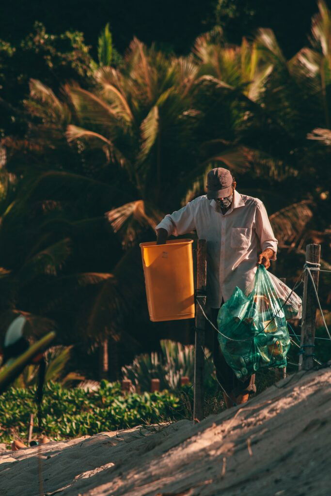 A man in a mask is cleaning up trash on the beach.