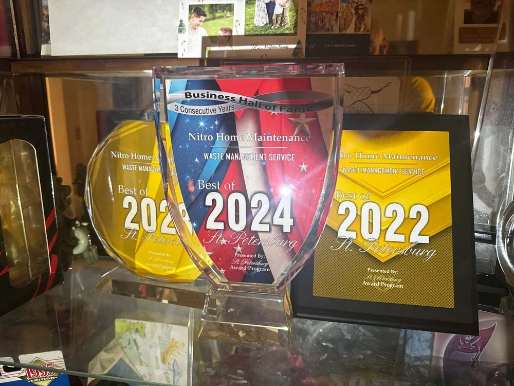 Three transparent acrylic awards on a shelf, labeled "best of Petersburg" for 2022, 2023, and 2024, recognizing excellence in home maintenance and junk removal services